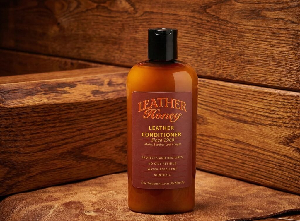 Alt Text: A bottle of Leather Honey Leather Conditioner, Since 1968 placed on a piece of treated brown leather to demonstrate its restorative and hydrating effects.